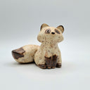 A small ceramic raccoon figurine with a speckled cream and brown glaze, sitting on a light gray background.