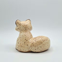 A small ceramic raccoon figurine with a speckled cream and brown glaze, sitting on a light gray background.