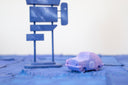 Pair of 2 carved wooden sculptures: a small retro looking purple car with 81 drawn on the side, and a large signpost with 7 different signs, though all painting like a dark blue night sky without any words.