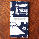 Folded fabric with white patterns on a blue background, featuring 'IKS Collection' branding, on a wooden surface.