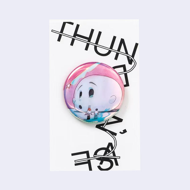 Circular pin with an illustration of a large head on a ground, with 2 small characters staring up at it.