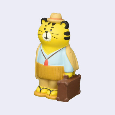 Small figure of a tiger dressed with a coat and hat, holding a brown luggage briefcase.