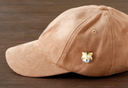 3D ceramic brooch/pin of a tiger's head, with small eyes, a cute smile and striping on its face. Shown on the side of a hat.