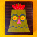 Painting of a green tiki head on a wooden panel.