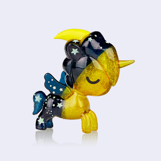 A small half starry blue night and half golden sparkly unicorn figure. Atop its head is a yellow crescent moon and its eye is closed, as if sleeping.