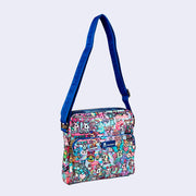 Small pouched shaped bag with an additional zipper section on the exterior. It has gold hardware details, and a cobalt blue sling strap attached. Bag is covered completely in a busy pastel color pattern featuring tokidoki characters with carnival food and drink imagery as well as carnival rides.