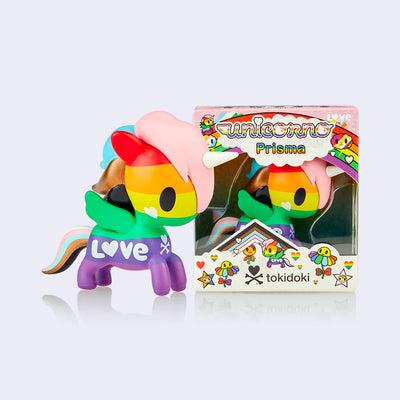 A vinyl unicorn colored like various pride flags, rainbow body with baby pink, blue, bronze and black hair. It stands next to its clear product packaging.