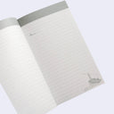 An open lined notebook with a light gray top border and a small gray illustration in the bottom-right corner, shown on a pale lavender background.