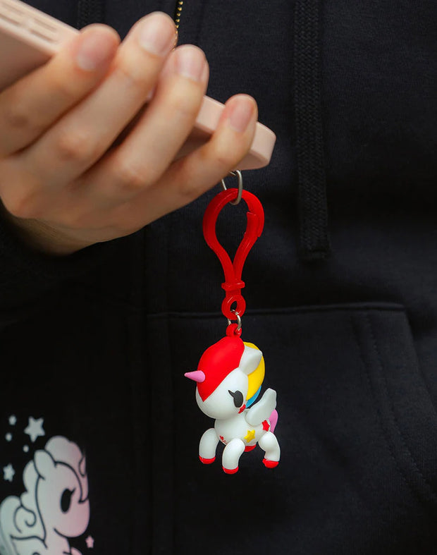 Small, soft PVC material bag charm of a white unicorn with a rainbow color mane. Charm is attached to a cell phone.