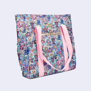Large tote bag, side angle. Features pastel pink colored fabric detailing, around the zipper and as the handles/straps. Bag has a small "tokidoki" nameplate on the upper center and is covered completely in a busy colorful pattern featuring tokidoki characters with with galactic and sci fi imagery.