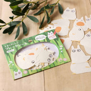 Packaged sticker sheet with cartoon chibi Totoro design on a wooden surface with green leaves.