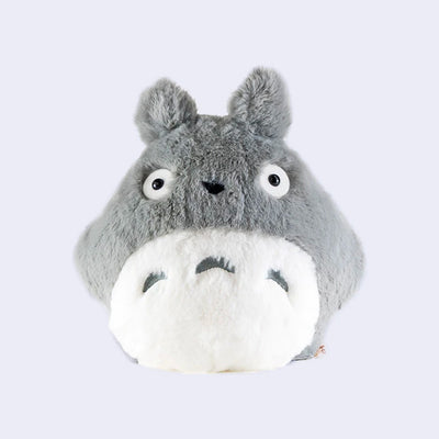Round, fluffy light grey Totoro plush with a round stomach and no mouth.