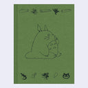 Green fabric hardcover journal with embossed illustrations of Totoro, sitting and faced to the side. Along the top and bottom are smaller nature themed doodles.