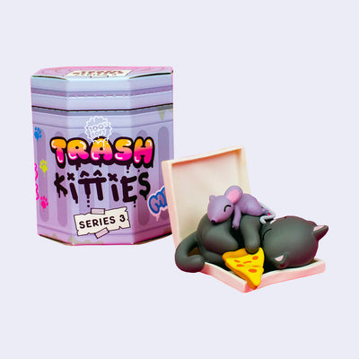 A small, plastic figurine of a black cat resting in an open pizza box, with a rat sleeping on its back and a slice of pizza in its paw. It stands next to its product packaging.