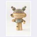 Photo print of a ceramic statue of a character with closed eyes, a small dress, ear cuffs and their hair up in space-like buns. On their arm is a small caterpillar and on their knee is a bandaid. 
