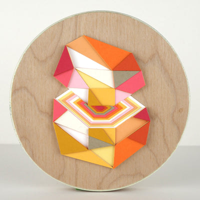 Geometric designed layered cut paper sculpture mounted on wood, creating a three dimensionality. A 10 sided shape is cut horizontally, revealing a hexagonal interior. Colors are orange, grey, yellow, pink and white.