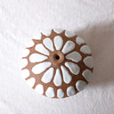 Small terracotta colored clay vase with large semi raised white ovals all around it, as a pattern.