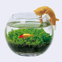A clear glass fishbowl filled with green aquatic plants and a small orange fish, with a ginger cat figurine leaning over the rim against a light gray background.