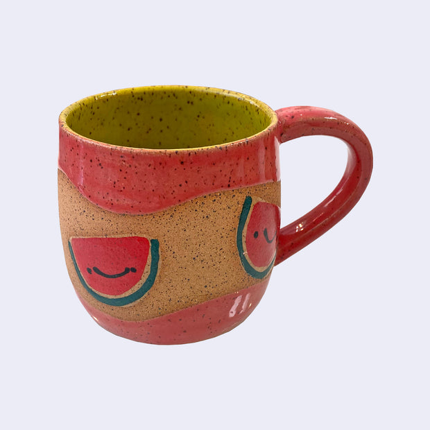 Ceramic mug with spotted finishing and an earthy brown exterior and lime green interior. On the outside are painted on cartoon style watermelons, with simple expressions.