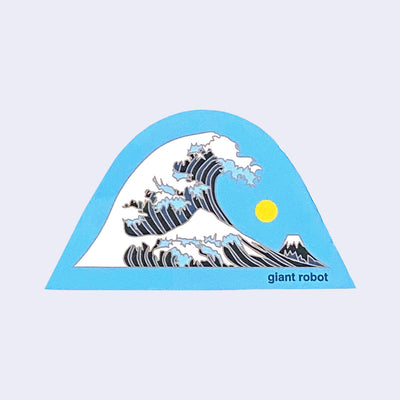 Die cut blue outlined sticker of a blue striped wave design, with white foam atop the waves, akin to Hokusai print "The Great Wave off Kanagawa." A yellow sun is in the sky and a small mountain can be seen in the background. "Giant Robot" is written in small font in lower right corner.