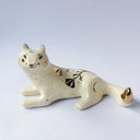 Cream colored ceramic sculpture of a wolf, lying down. It has a gold luster poppy flower design on its back and gold accents on its tail, chest and head.