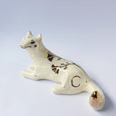 Cream colored ceramic sculpture of a wolf, lying down. It has a gold luster poppy flower design on its back and gold accents on its tail, chest and head.