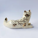Cream colored ceramic sculpture of a wolf, lying down. It has a gold luster poppy flower design on its back and gold accents on its tail, chest and head.