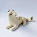 Cream colored ceramic sculpture of a wolf, lying down. It has a gold luster poppy flower design on its back and gold accents on its tail, chest and head.