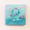 A square hand-painted canvas featuring a cute light blue puppy sitting in grass with pink clouds against a light blue sky. It holds a shiny pink ball in its hand.