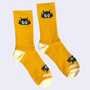 Goldenrod yellow socks with an olive green cartoon robot head on them and cream colored heels and toes. The robot head decorates the cuff end of each sock so that it peeks out when you wear sneakers.