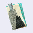 Rectangular cream colored towel with a bright blue border with illustrations of mountains and a blue snow yeti, standing atop of one with its arms up. Close up showing embroidered details.