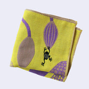 Light yellowish green square handkerchief featuring stylistic illustrations of a purple plant, with a very thick trunk and bulb shaped blooms. A small black frog jumps onto one of the blooms. Folded.
