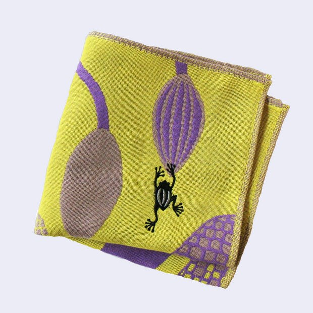 Light yellowish green square handkerchief featuring stylistic illustrations of a purple plant, with a very thick trunk and bulb shaped blooms. A small black frog jumps onto one of the blooms. Folded.