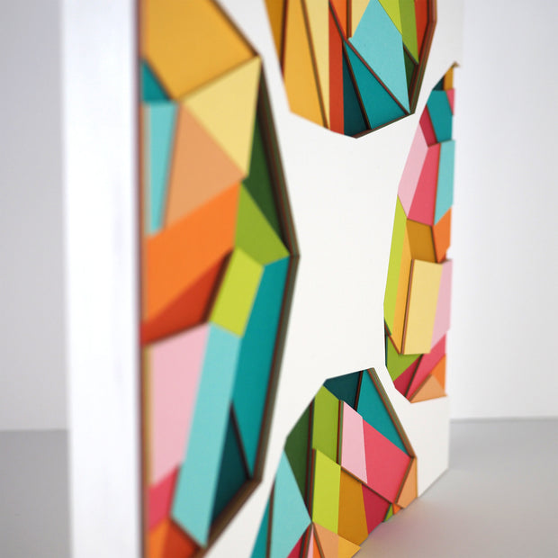 White paper with 4 colorful geometric shapes on each side of the sheet, made up of layers of colorful paper assembled into a larger geometric shape. Shown at the side to display 3 dimensionality