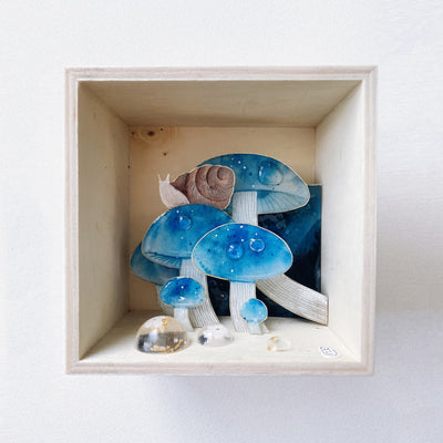 Open wooden shadow box, featuring a set of paper cut out sculptures of blue mushrooms with water droplets on them and the floor. A brown snail sits on one of the mushrooms.