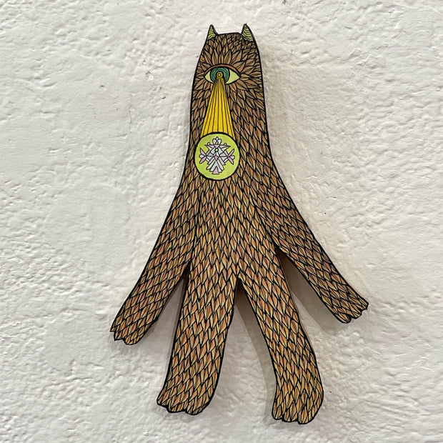 Illustrated wood cut of a tall patterned cyclops with small horns who beams a yellow light and geometric pattern out of its eye.