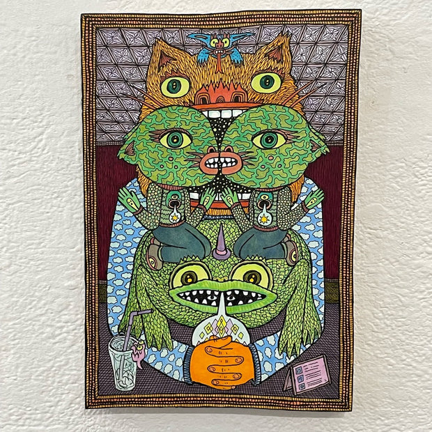Illustration on wood with a patterned border. A large monster sits with his hands clasped on a table with a place card and glass of water. Two kissing green goblins are sitting on a frog with a wizard hat. 