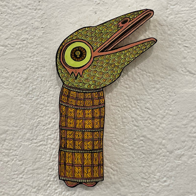 Illustrated wood cut of an amphibian like creature with a large green eye. It wears a full body wrap with a detailed geometric pattern.