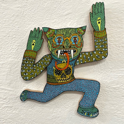 Illustrated wood cut of a green cat-like monster with gold glasses and small monsters as eyes. It wears a sweater vest with a skull over a long sleeve with eyeball pattern. 