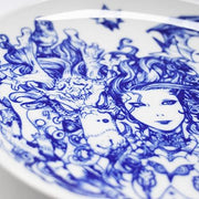 Close up of plate featuring a woman with long, wavy hair and mechanical body, one hand lightly touching a dragon head, with another dragon is on her opposite side.