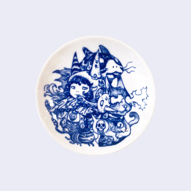 Small white ceramic plate with deep blue intricate line art. Plate features a small girl surrounded by a cat shooting white static out of its eyes and other animals and animal masks.