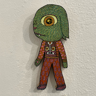 Illustrated wood cut of a timid looking large eye goblin with long droopy ears. It wears a pink and orange patterned sweater and pants.