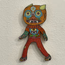 Illustrated wood cut of a horned orange goblin with two smaller monsters kissing making up its face. It wears a bright orange and red patterned outfit with two monsters on its sweater.