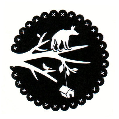 Black circular paper cutting of a wolf standing on a single tree branch, with a small house attached by a string. 