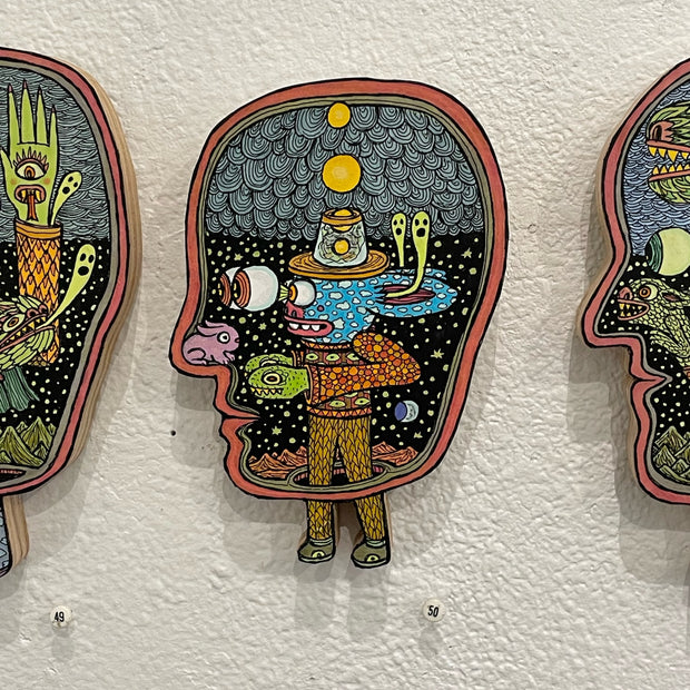 Illustrated wood cut of a human head, facing left. Inside is a blue rabbit-like monster looking through large eyes, wearing a hat with yellow globes within it. A small pink bunny sits on the interior of the human's nose.