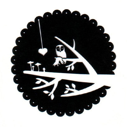 Black circular paper cutting of a single tree branch with an owl perched. Small leaves and mushrooms come out from the branch, a heart on a string hangs down into the scene.