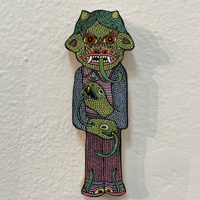 Illustrated wood cut figure of a horned green goblin with dragon heads for hands wearing a patterned sweater vest and shoes that have eyes and tongues.
