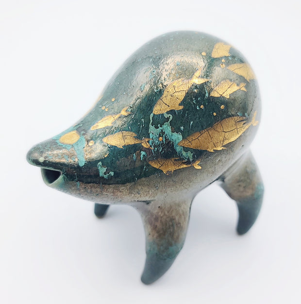 Rounded deep teal ceramic sculpture of a quadruped with a wide goofy smile. Gold fish swim on its body with splatters of blue. 