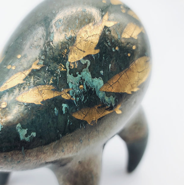 Rounded deep teal ceramic sculpture of a quadruped with a wide goofy smile. Gold fish swim on its body with splatters of blue.