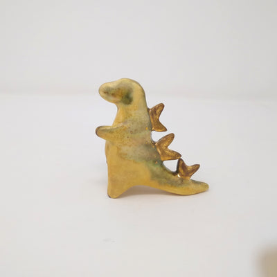 A small ceramic yellow and green Godzilla figure, with no facial features and minimal body details. It has abstract gold spikes on its back.